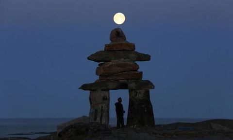 A man looks at a giant inukshuk as the moon rises above it in Rankin Inlet, Nunavut in this file photo from August 21, 2013.