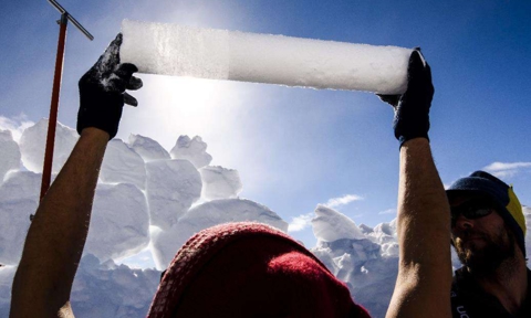 Alun Hubbard holds up a section of the ice core. The visible divide between superimposed ice on the left and snow firn on the right reveals hot summer melt and refreezing events.
